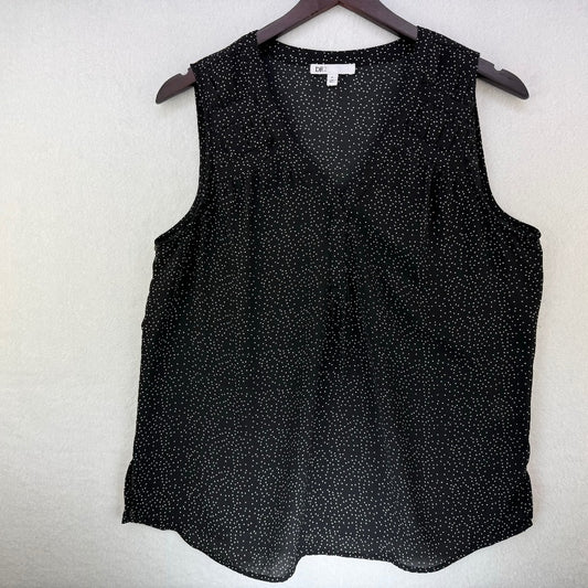 A sleeveless black V-neck blouse with a small white speckled pattern, hanging on a dark wooden hanger against a textured off-white wall.