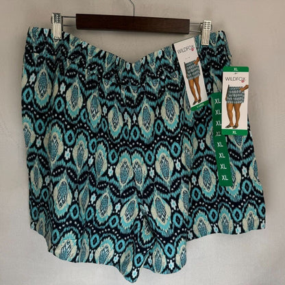 A pair of women's shorts with a teal, black, and white ikat pattern, hanging on a wooden hanger with retail tags attached. The brand 'WildFashion' is visible on the tags.
