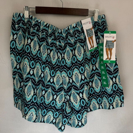 A pair of women's shorts with a teal, black, and white ikat pattern, hanging on a wooden hanger with retail tags attached. The brand 'WildFashion' is visible on the tags.