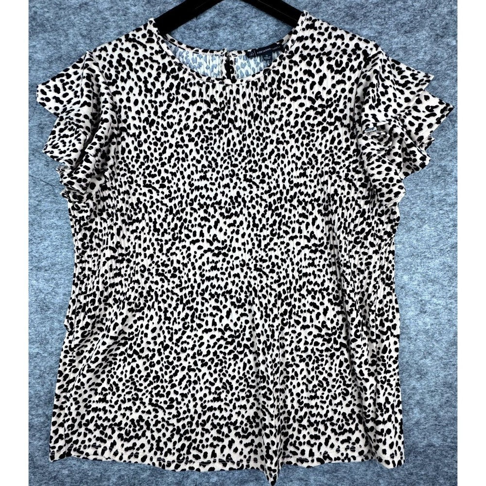 A black and white leopard print short-sleeve blouse with ruffled sleeves, hanging on a black hanger against a textured blue-gray background.