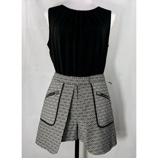 A sleeveless black top paired with a black and white patterned asymmetrical skirt featuring zippered pockets, displayed on a mannequin against a white backdrop.