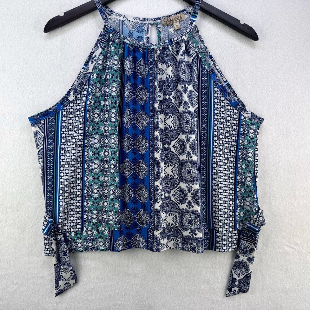 A sleeveless halter-style top with a multicolor bohemian print in blue, navy, green, and white, hanging on a black hanger against a textured white wall.