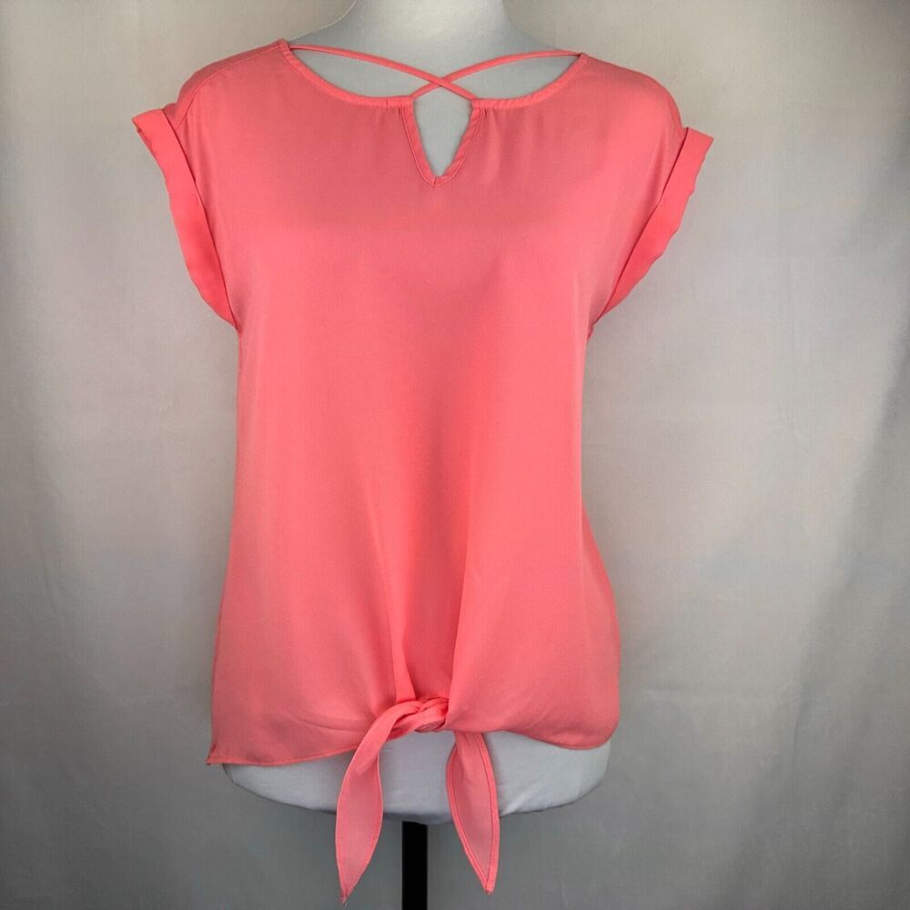 A coral pink short-sleeve blouse with a keyhole back and front tie detail, displayed on a white mannequin torso against a light gray fabric backdrop.