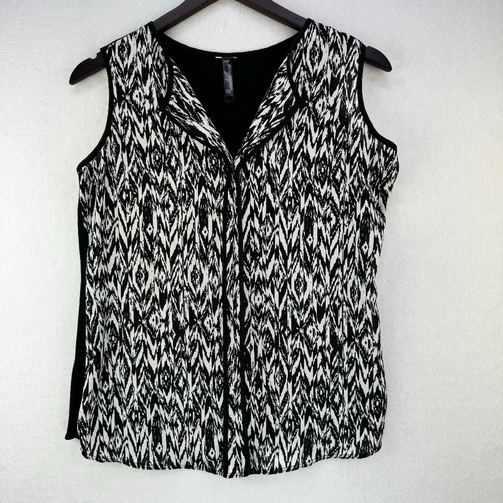 A sleeveless black and white patterned vest with a V-neckline, hanging on a dark wooden hanger against a light textured wall.