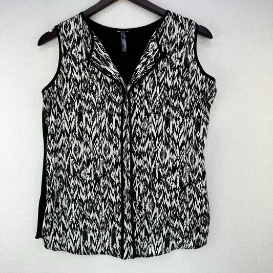 A sleeveless black and white patterned vest with a V-neckline, hanging on a dark wooden hanger against a light textured wall.