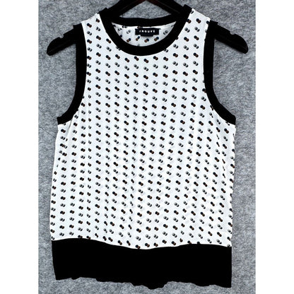 A sleeveless white knit top with a black dotted pattern, black trim, and a black ruffled hem, hanging on a black hanger against a gray textured background.