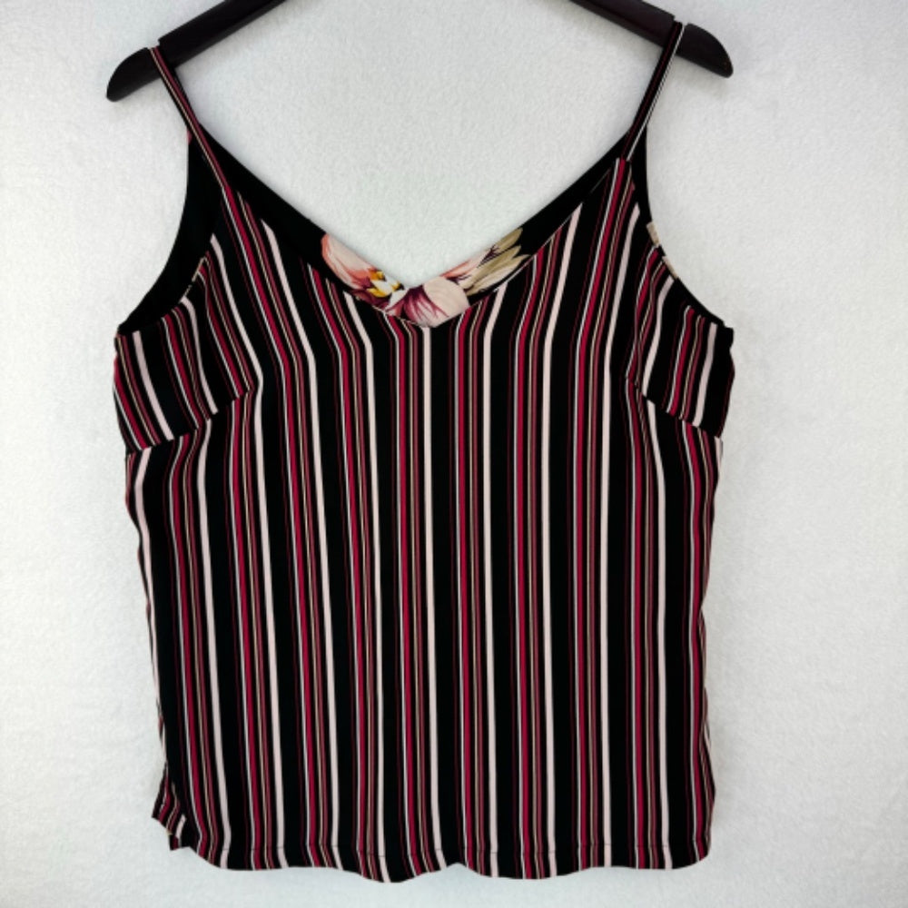 A sleeveless striped camisole top hanging on a black hanger against a white textured wall. The top features vertical stripes in black, white, and red, with a small floral accent at the V-neckline.
