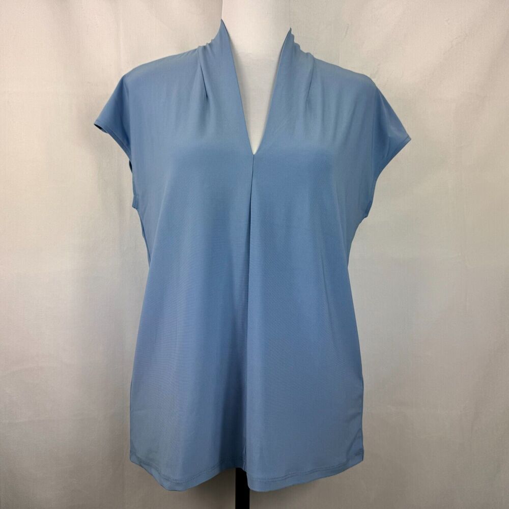A light blue short-sleeve blouse with a split V-neckline, displayed on a mannequin torso against a light gray fabric backdrop.