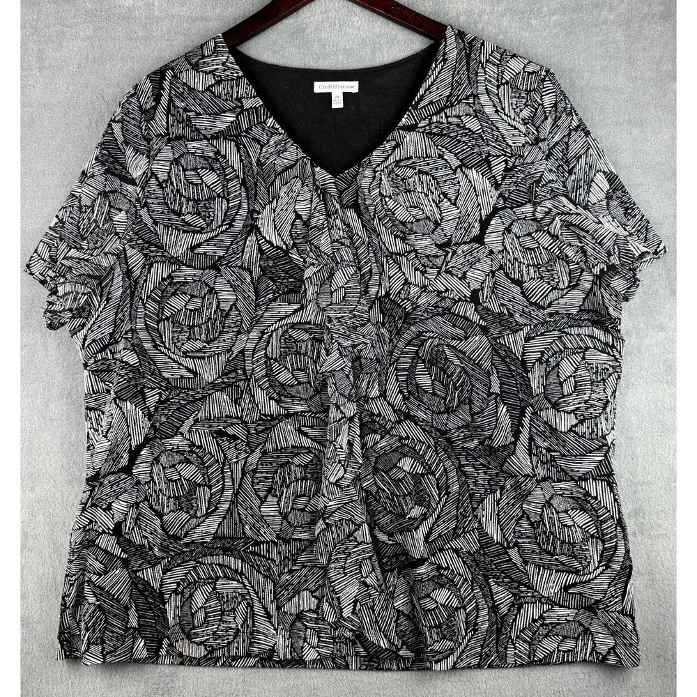 A short-sleeve V-neck blouse with an all-over black and gray abstract line pattern, hanging on a dark wooden hanger against a textured gray background.