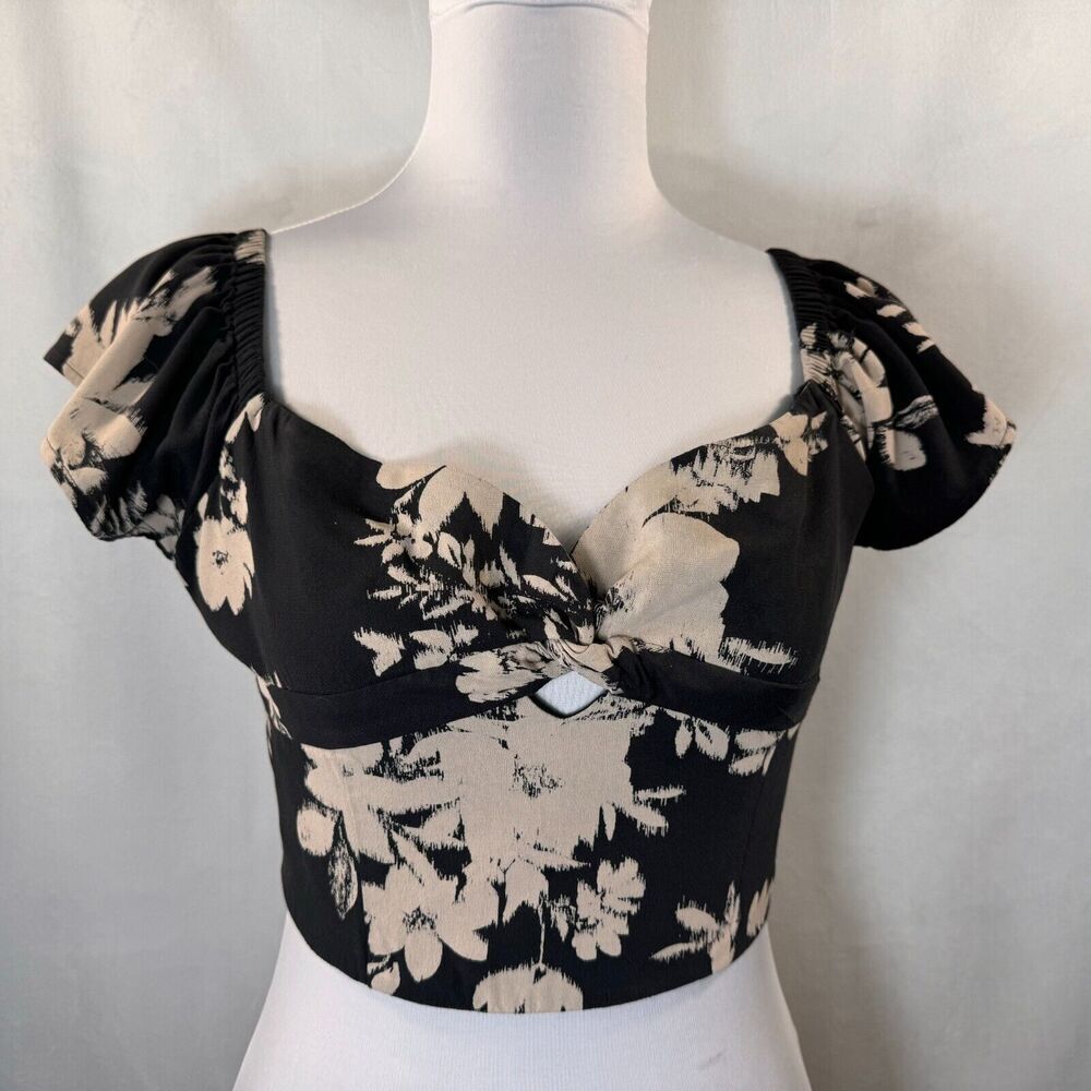 A black and beige floral print blouse with puff sleeves and a sweetheart neckline, displayed on a white mannequin torso against a light gray fabric backdrop.