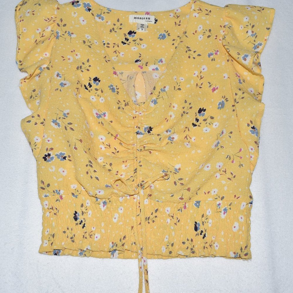 A yellow floral crop top with ruffled cap sleeves, a gathered front, and a drawstring tie at the waist, laid flat on a white background.