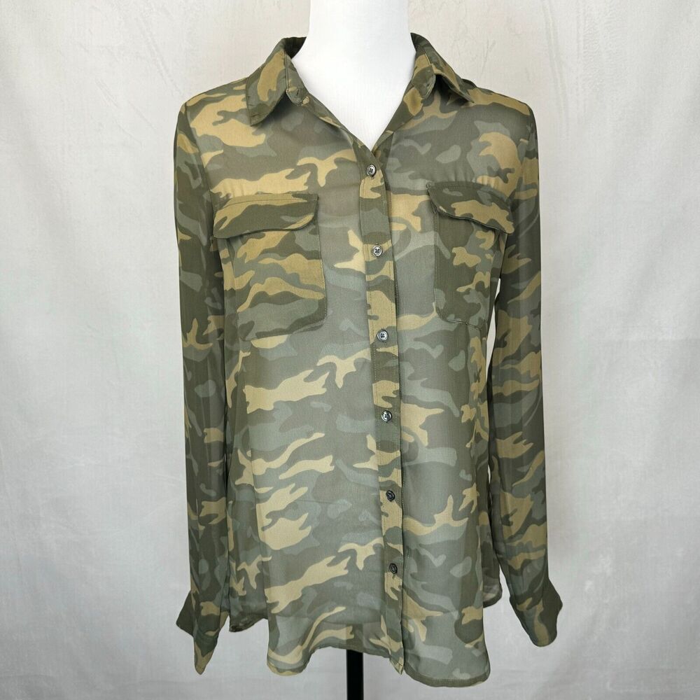 A long-sleeve button-up shirt with a green and tan camouflage pattern, displayed on a white mannequin torso against a light gray fabric backdrop.