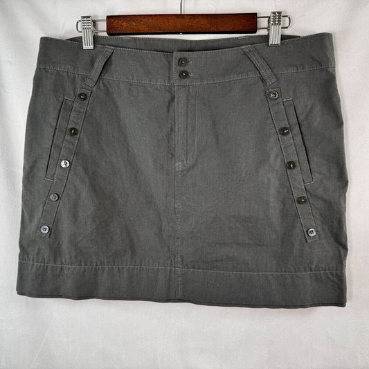 A gray mini skirt with buttoned side pockets, hanging on a wooden hanger against a white fabric background.