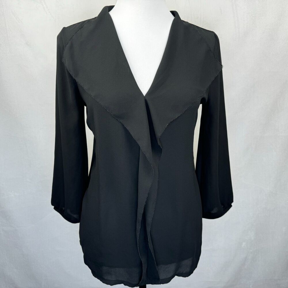 A black wrap-style blouse with three-quarter sleeves and a draped asymmetrical front, displayed on a white mannequin torso against a light gray fabric backdrop.