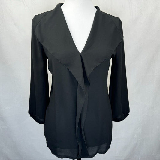 A black wrap-style blouse with three-quarter sleeves and a draped asymmetrical front, displayed on a white mannequin torso against a light gray fabric backdrop.