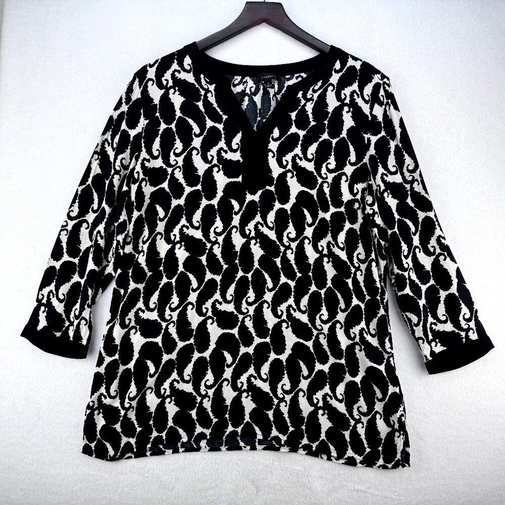 A black and white patterned long-sleeve top with a split V-neckline, hanging on a dark wooden hanger against a light gray textured background.