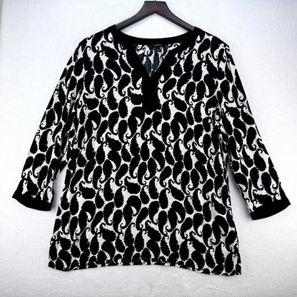 A black and white patterned long-sleeve top with a split V-neckline, hanging on a dark wooden hanger against a light gray textured background.
