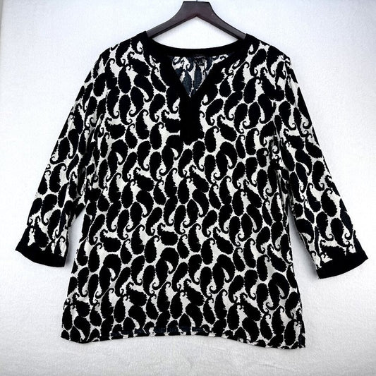 A black and white patterned long-sleeve top with a split V-neckline, hanging on a dark wooden hanger against a light gray textured background.