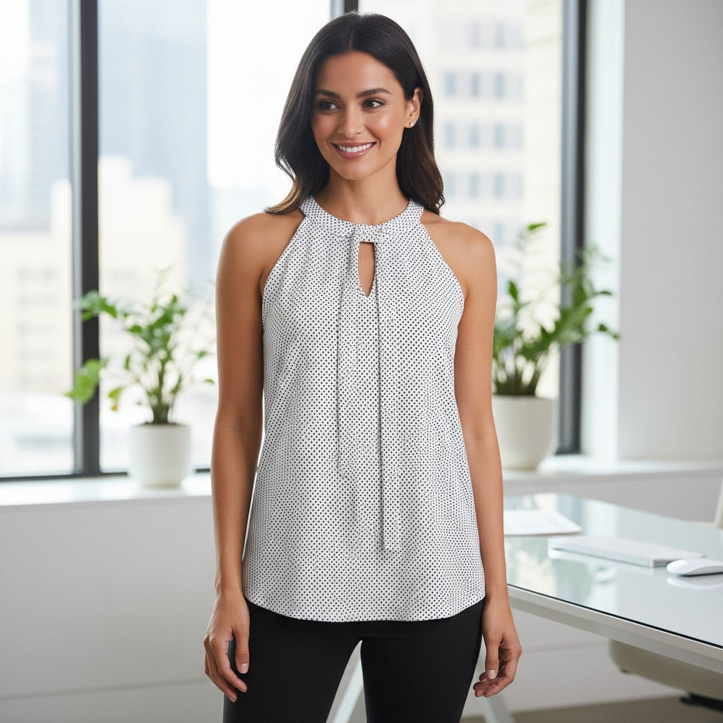 A woman modeling a sleeveless halter-neck top with a small black and white geometric pattern and a front keyhole cutout, standing in a bright modern office setting.