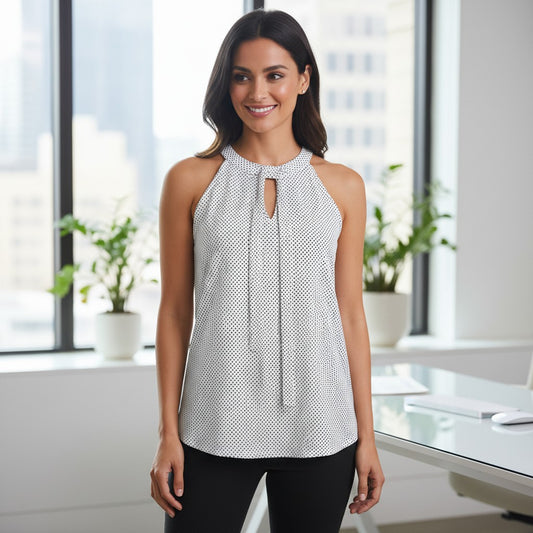 A woman modeling a sleeveless halter-neck top with a small black and white geometric pattern and a front keyhole cutout, standing in a bright modern office setting.