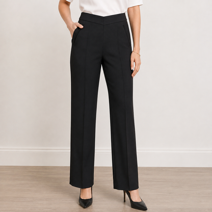 A model wearing black wide-leg trousers with a white top and black heels, standing against a neutral beige wall and light wood floor.