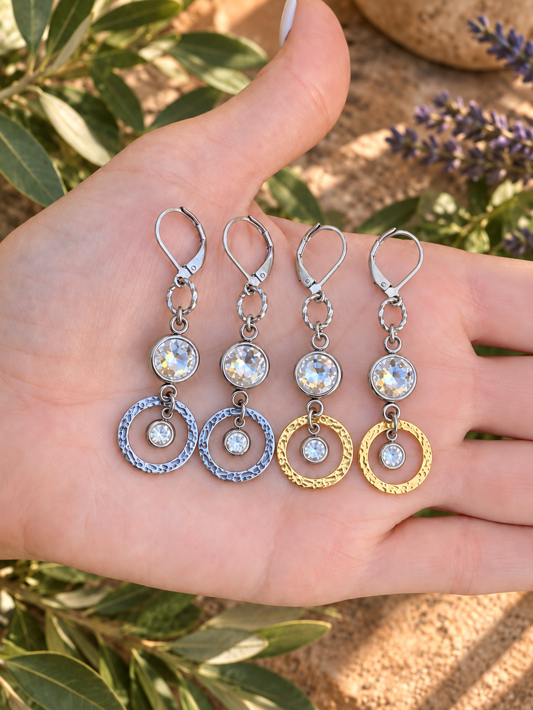 Hand holding silver and gold Venus Sunlight earrings showing rhinestone accents and textured circular drops.