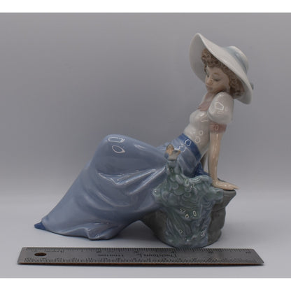 Left view of Lladro porcelain figurine of a woman in a blue dress and white hat and ruler for width