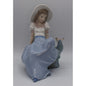Main view Lladro porcelain figurine of a girl in a blue dress and white hat sitting on a rock with a butterfly.