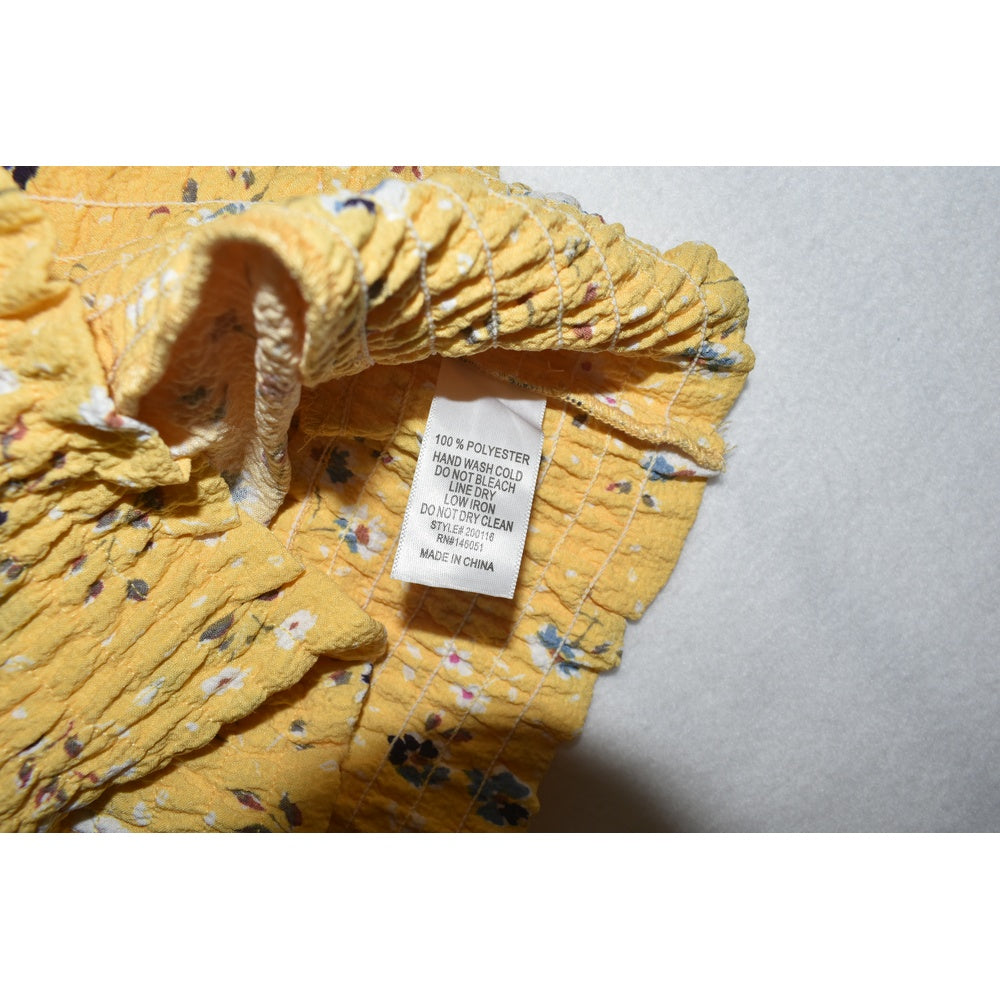 Clothing care material tag on Monteau crop top yellow floral fabric on a gray background