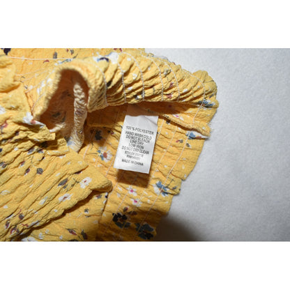 Clothing care material tag on Monteau crop top yellow floral fabric on a gray background