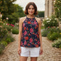 A woman stands in a garden wearing a sleeveless halter top with a navy blue background and a vibrant floral print in pink, red, and orange, paired with white shorts.
