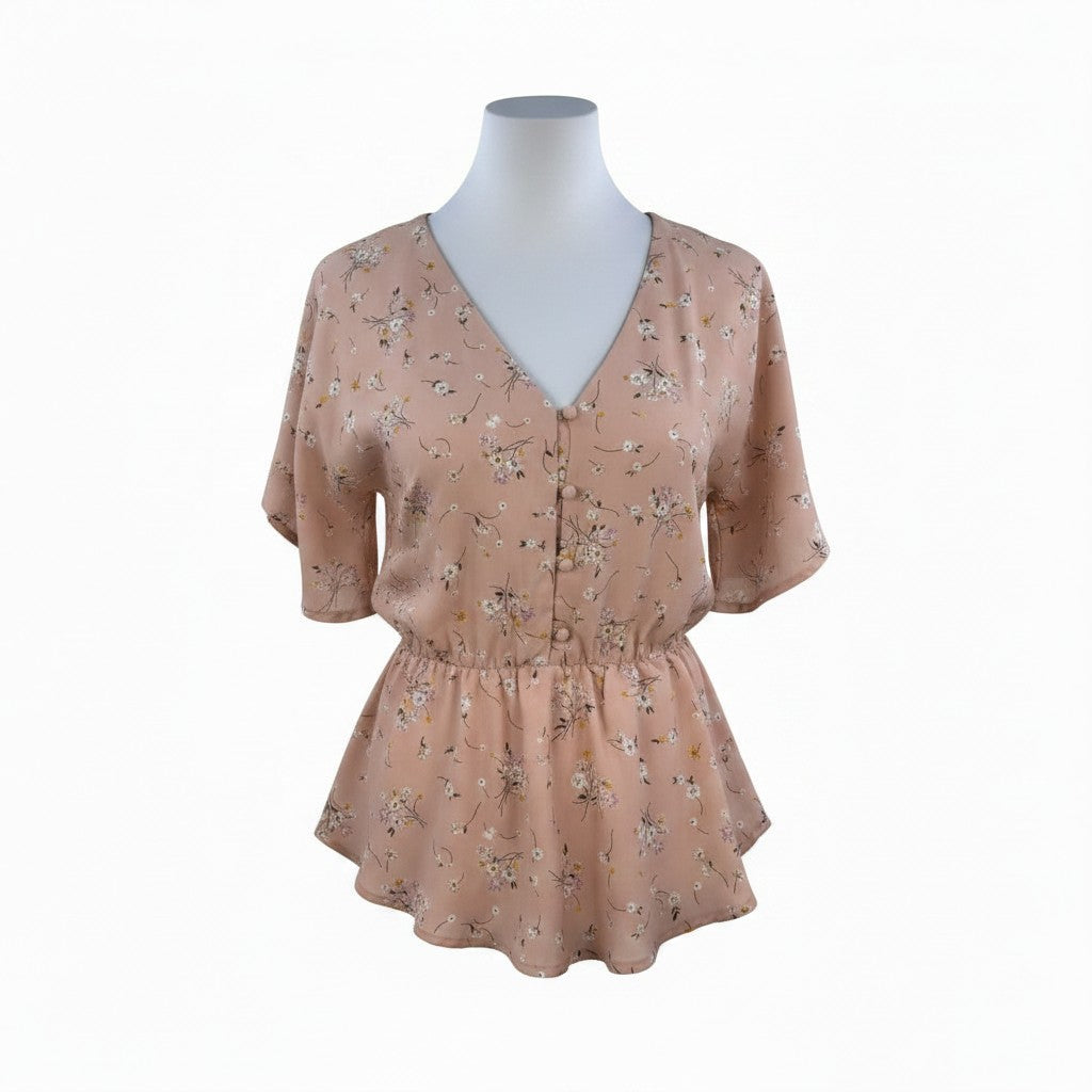 A short-sleeve V-neck blouse with a gathered peplum waist, featuring a delicate floral print in muted pink, beige, and green tones. The blouse is displayed on a white mannequin torso against a plain white background.