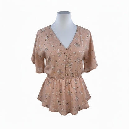 A short-sleeve V-neck blouse with a gathered peplum waist, featuring a delicate floral print in muted pink, beige, and green tones. The blouse is displayed on a white mannequin torso against a plain white background.