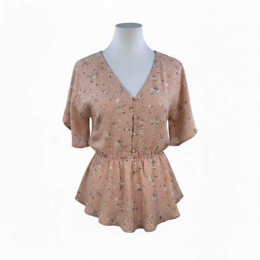 A short-sleeve V-neck blouse with a gathered peplum waist, featuring a delicate floral print in muted pink, beige, and green tones. The blouse is displayed on a white mannequin torso against a plain white background.