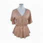 A short-sleeve V-neck blouse with a gathered peplum waist, featuring a delicate floral print in muted pink, beige, and green tones. The blouse is displayed on a white mannequin torso against a plain white background.