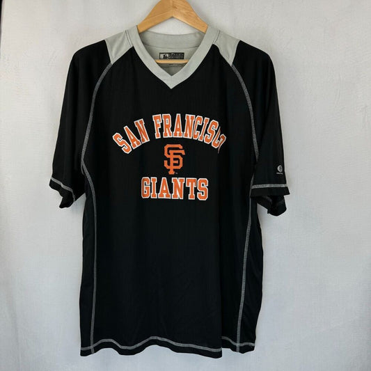 A black San Francisco Giants baseball jersey hanging on a wooden hanger against a white wall. The jersey features a gray V-neck collar, gray sleeve cuffs, and gray piping details, with 'SAN FRANCISCO GIANTS' and the 'SF' logo printed in orange and white on the front.