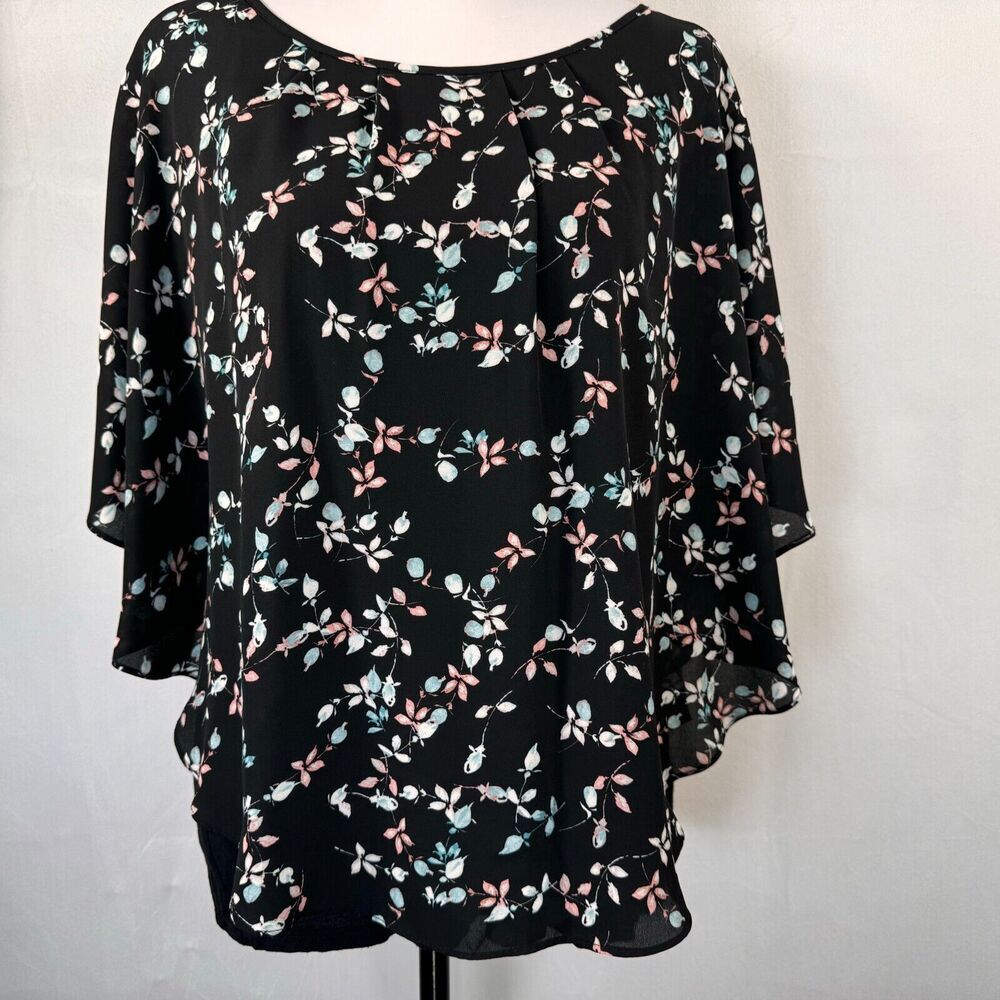A black three-quarter sleeve blouse with a delicate pink, light blue, and white floral print, displayed on a mannequin torso against a light gray background.