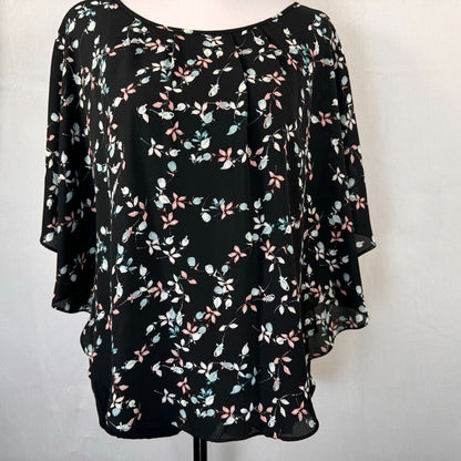 A black three-quarter sleeve blouse with a delicate pink, light blue, and white floral print, displayed on a mannequin torso against a light gray background.