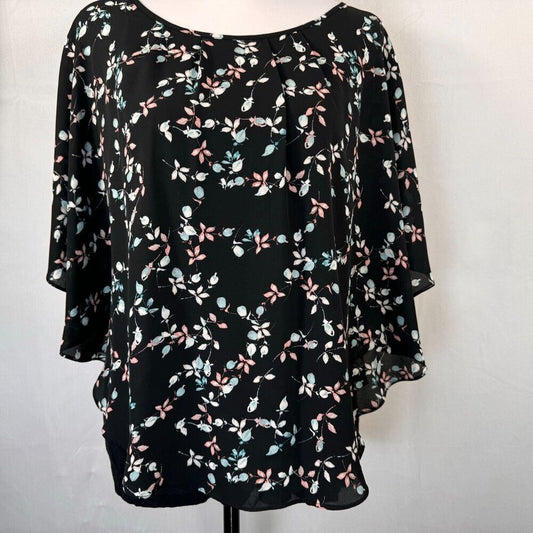 A black three-quarter sleeve blouse with a delicate pink, light blue, and white floral print, displayed on a mannequin torso against a light gray background.