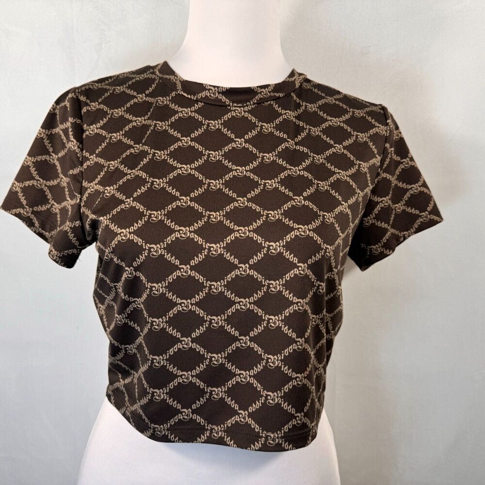 A brown short-sleeve crop top with a beige interlocking G pattern, displayed on a white mannequin torso against a light gray background.