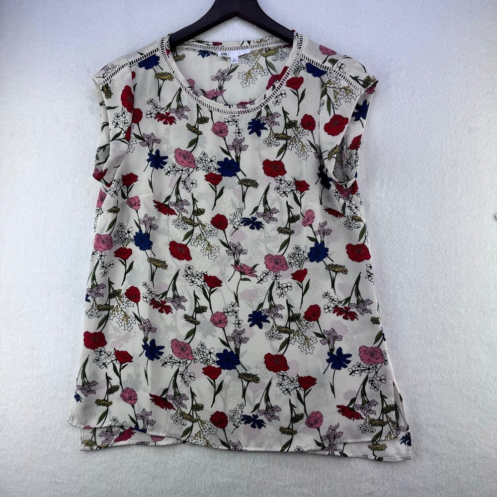 A sleeveless white top with a dense multicolor floral print, hanging on a black hanger against a textured white wall.