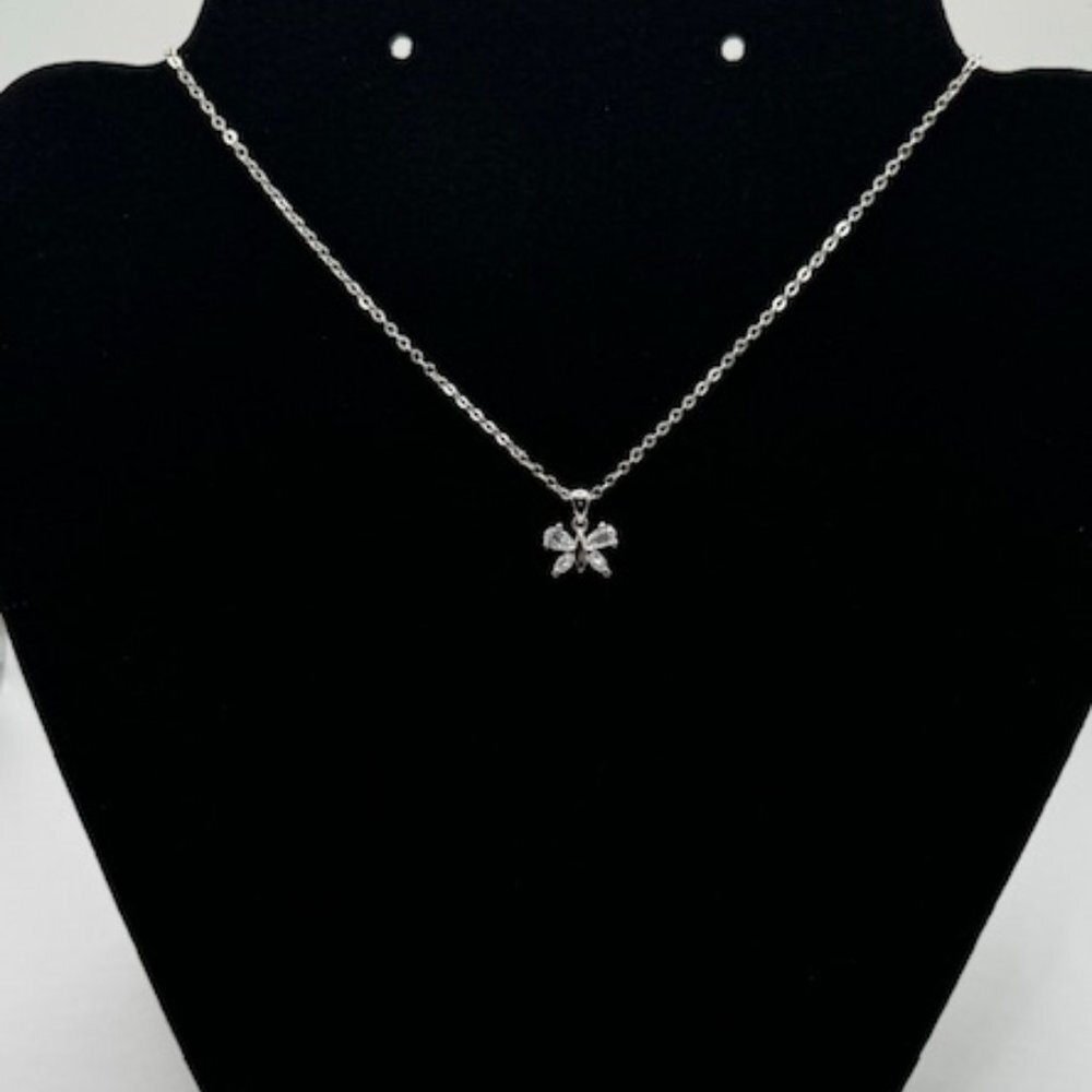 A silver chain necklace with a small bow-shaped pendant set with clear stones, displayed on a black jewelry bust.