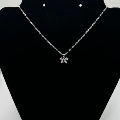 A silver chain necklace with a small bow-shaped pendant set with clear stones, displayed on a black jewelry bust.