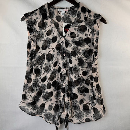 A sleeveless button-front blouse with a black floral and botanical print on a light beige background, hanging on a black hanger against a white fabric backdrop.