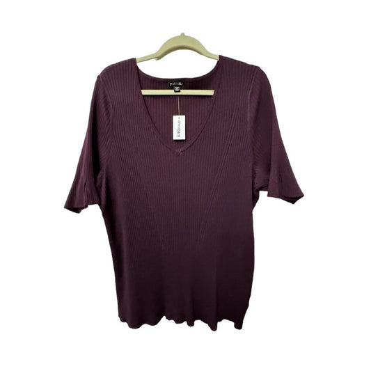 A women's short-sleeve ribbed knit top in deep plum purple, hanging on a light wood hanger against a plain white background. The brand 'Bella+Canvas' is visible on the neck label and hangtag.