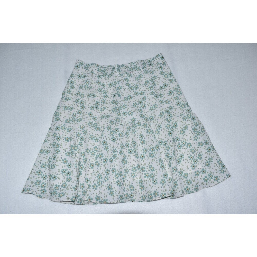 A white A-line skirt with a green floral pattern, laid flat against a light gray background.