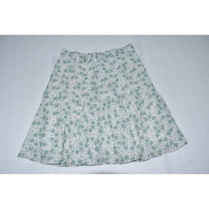A white A-line skirt with a green floral pattern, laid flat against a light gray background.