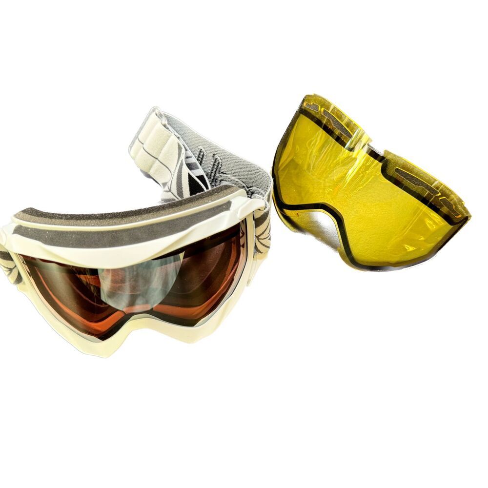 A pair of motocross goggles with a white frame and a yellow tinted lens, shown alongside a separate yellow lens on a plain white background.