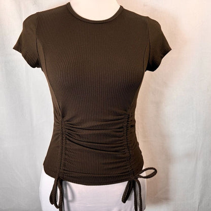 A dark brown ribbed short-sleeve crop top with a ruched side detail and drawstring ties, displayed on a mannequin torso against a light gray fabric backdrop.