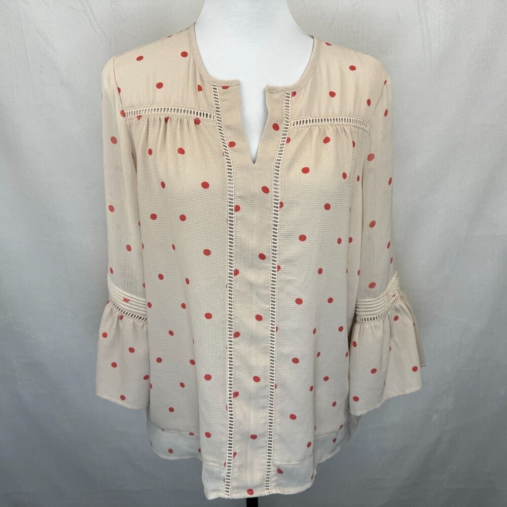A cream-colored blouse with red polka dots and decorative stitching, displayed on a white mannequin torso against a gray fabric backdrop.